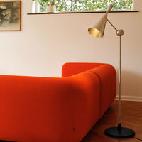 Bright orange curved sofa with smooth texture, complemented by a sleek standing lamp against a light wall.