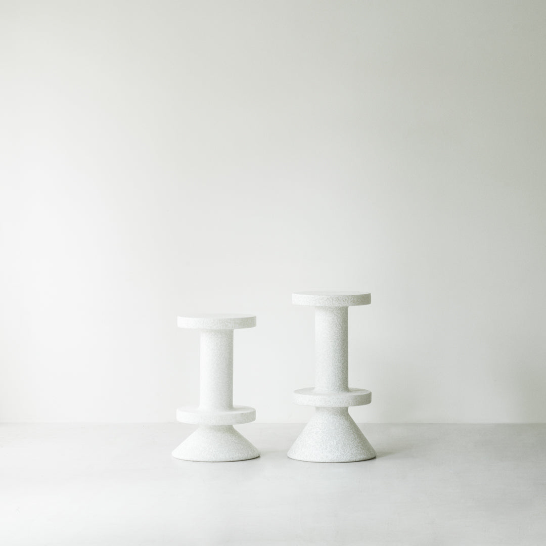 Two modern white stools with geometric shapes against a minimalist backdrop.