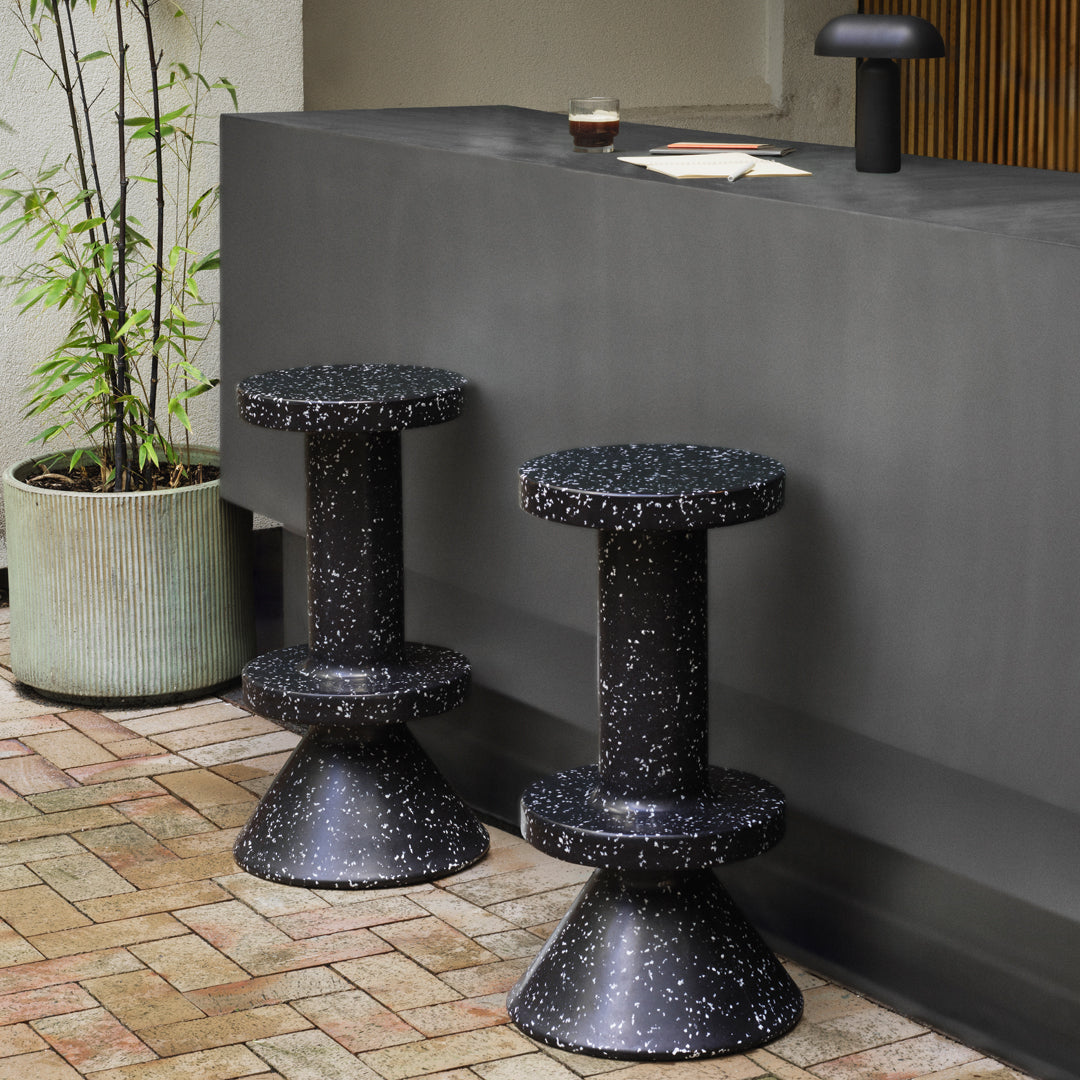 Black terrazzo-style stools with speckled patterns, set against a sleek dark countertop. Modern, minimalist aesthetic.
