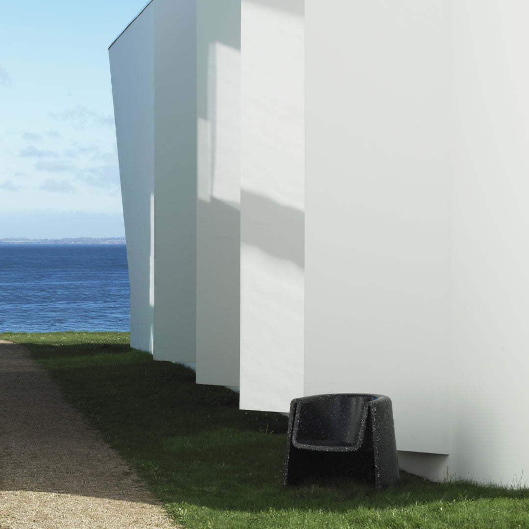Black textured chair against a backdrop of white architecture and blue ocean, complemented by green grass.