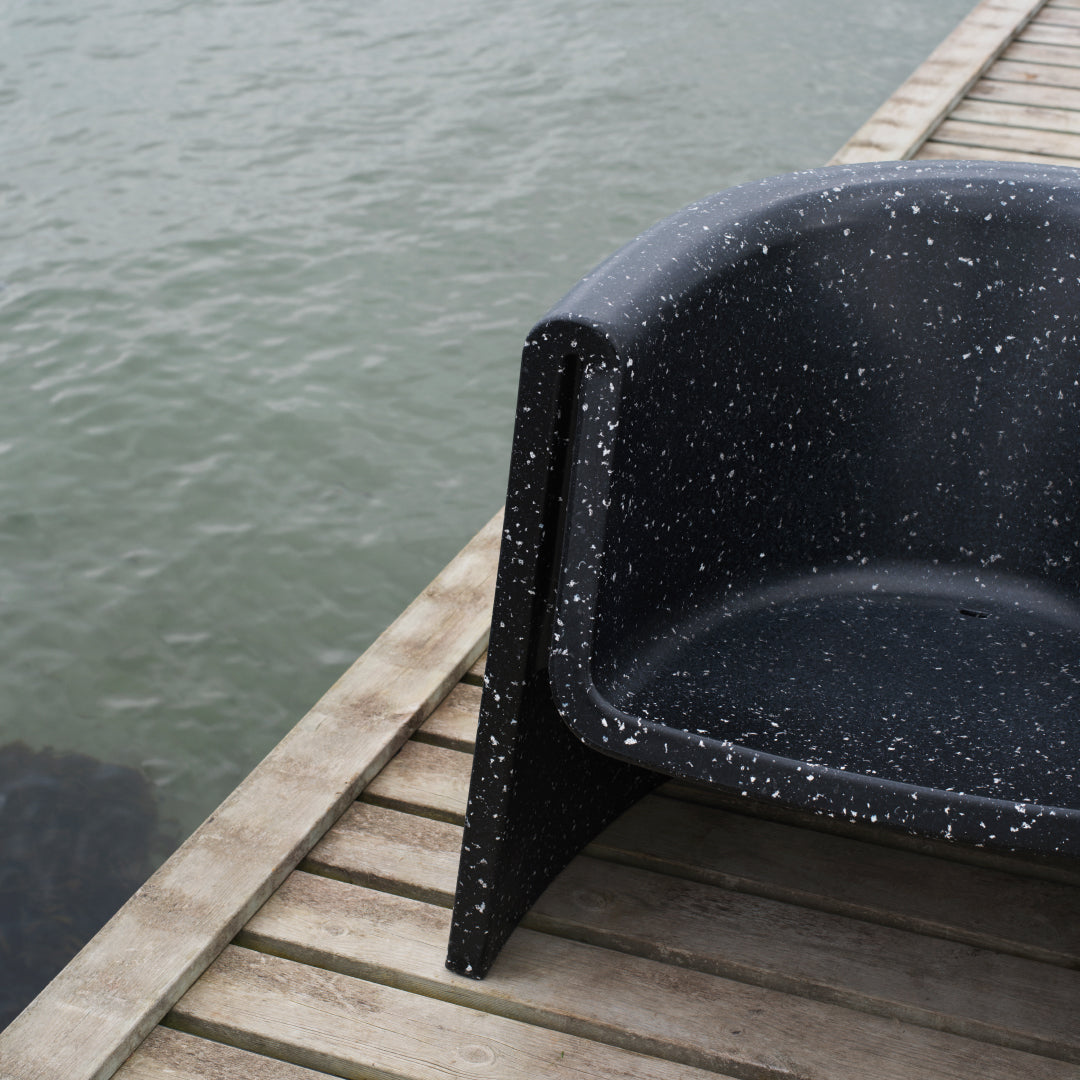 Black chair with a speckled pattern, featuring white flecks against a matte finish, set near water.