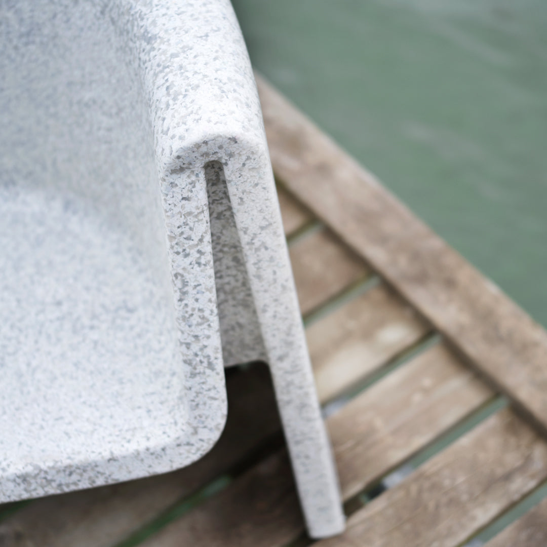 Textured grey speckled chair with smooth edges against a wooden backdrop, highlighting modern design.