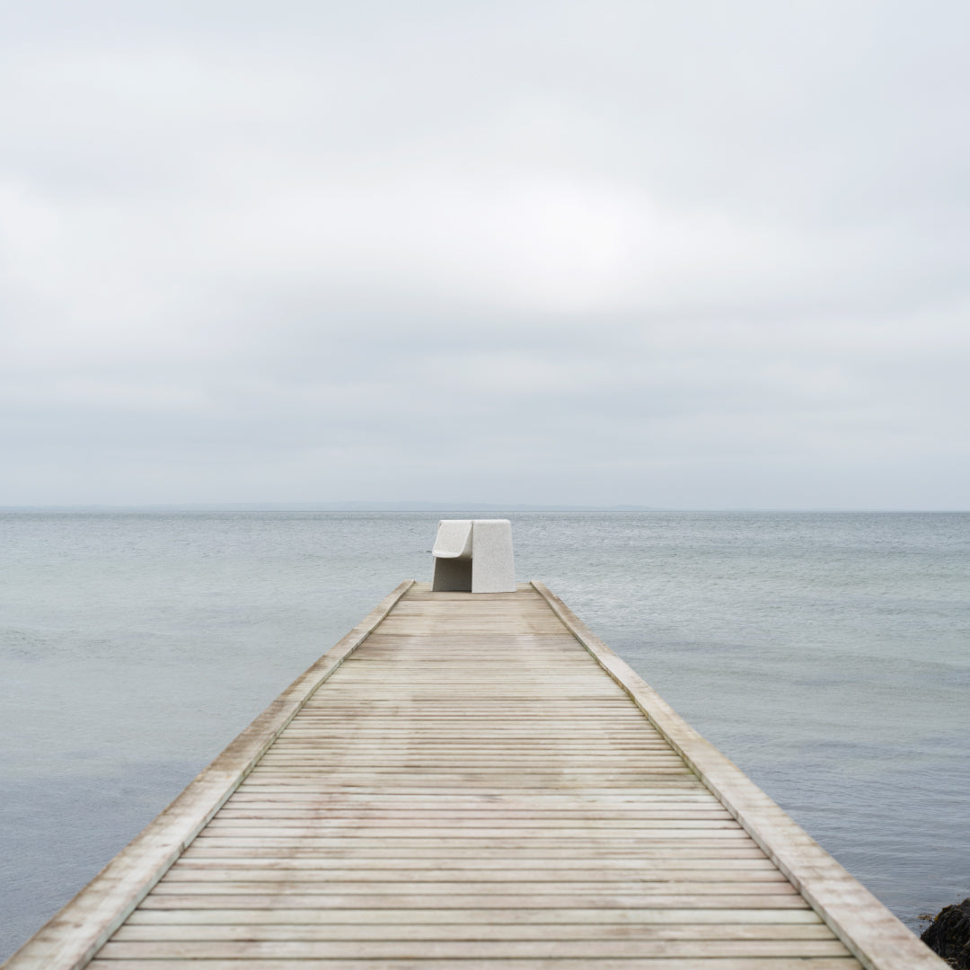 Wooden pier extending over calm gray waters under a light gray sky, creating a serene, muted color palette.