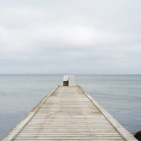 Wooden pier extending over calm gray waters under a light gray sky, creating a serene, muted color palette.