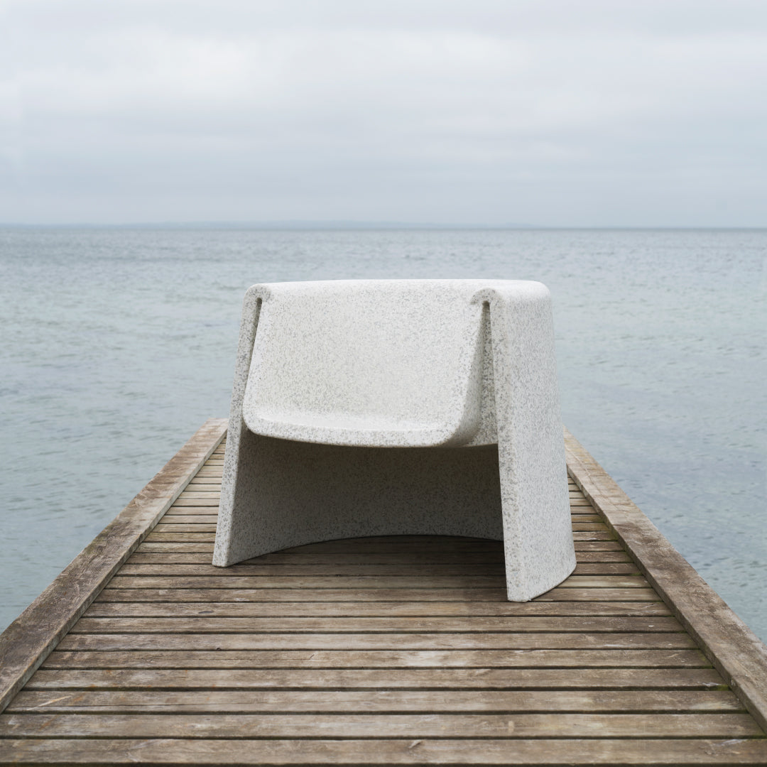 White textured chair with a smooth finish, set against a serene coastal backdrop. Perfect for modern outdoor aesthetics.