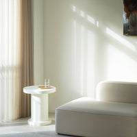 White minimalist side table with a smooth finish, complemented by soft beige curtains and a light gray rug.