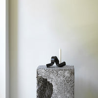 Black decorative ribbon on a textured gray pedestal with a white candle against a minimalist light background.