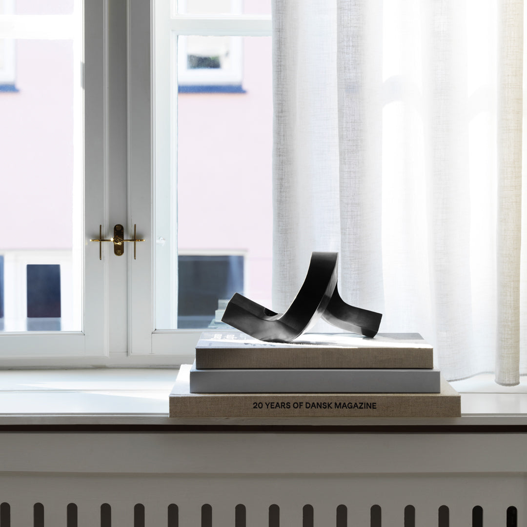 Black abstract sculpture on stacked books, with soft natural light filtering through sheer curtains. Stylish minimalism.