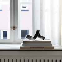 Black abstract sculpture on stacked books, with soft natural light filtering through sheer curtains. Stylish minimalism.