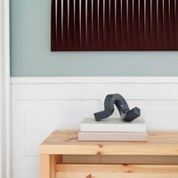 Dark gray abstract sculpture on stacked light-colored books against a muted mint green wall and burgundy artwork.