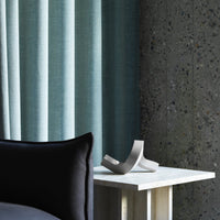 Light blue textured curtains with a black accent pillow and a minimalist white table against a speckled grey wall.