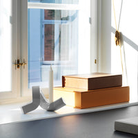 "Stacked boxes in warm orange and brown hues beside a white candleholder on a sunlit windowsill."