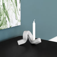 Silver wave-shaped candle holder on a dark surface, with a white candle, against a green abstract background.