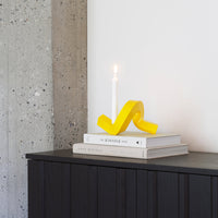 Bright yellow candle holder with a wavy design, set against neutral gray and white tones, stacked on white books.