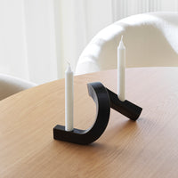 Modern black candle holder with minimalist design, featuring white candles on a light oak table.