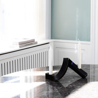Elegant black candle holder with a modern curved design and two white candles, set on a sleek marble table.