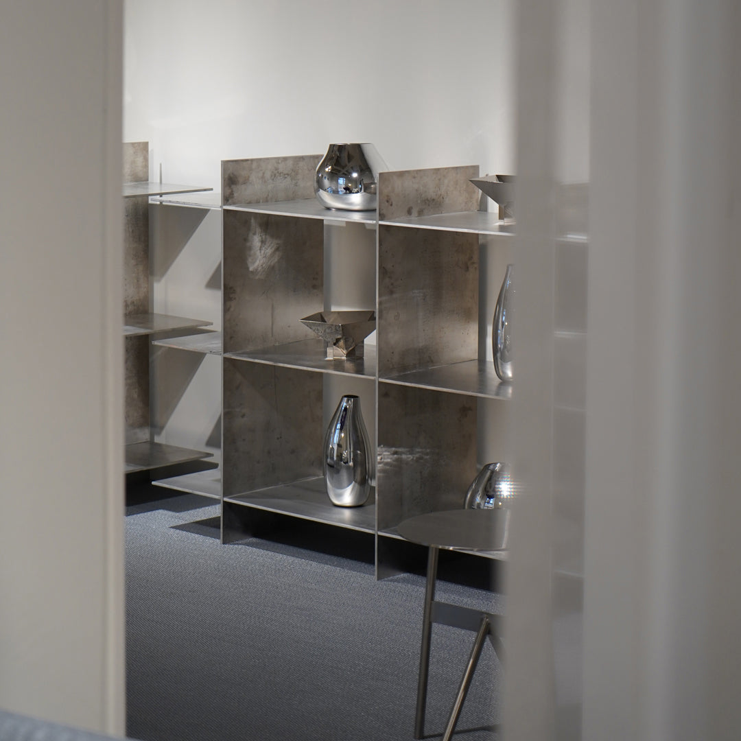 Sleek silver shelves with shiny metallic vases create a modern, minimalist aesthetic against a soft gray backdrop.