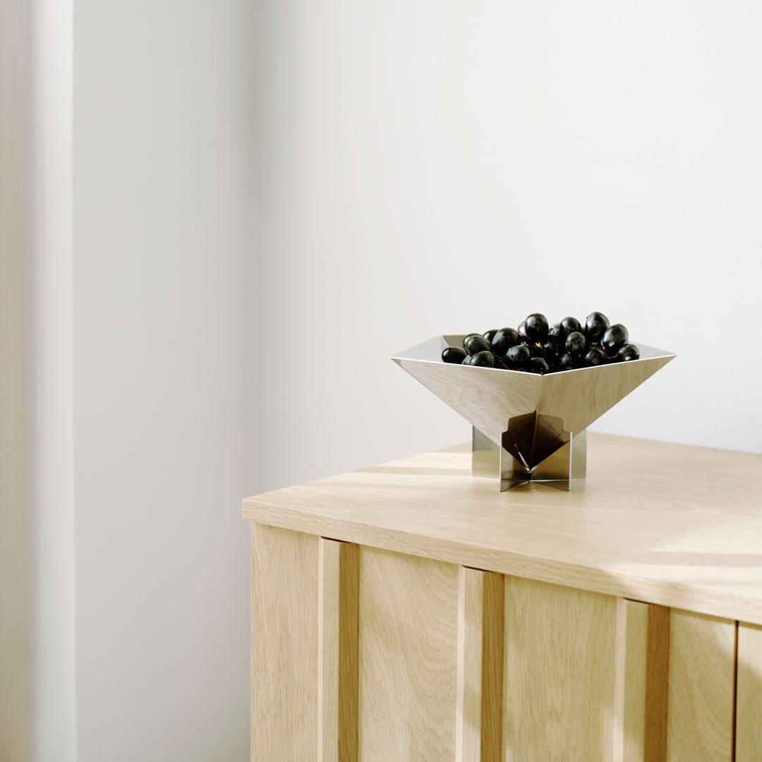 "Modern silver bowl with a sleek geometric design, showcasing a contrast of shiny metal and dark fruits."