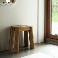 Natural wood grain stool in a light oak finish, minimalist design with smooth edges, placed against a neutral wall.