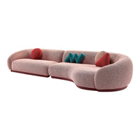 Curvy pink sofa with textured fabric, complemented by red and teal cushions, featuring a maroon base.
