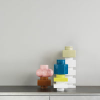 Colorful stacked vases featuring pink, brown, blue, yellow, and white geometric patterns against a neutral background.