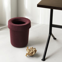 Burgundy felt waste bin with a rounded top, situated beside a black metal table on a light gray floor.