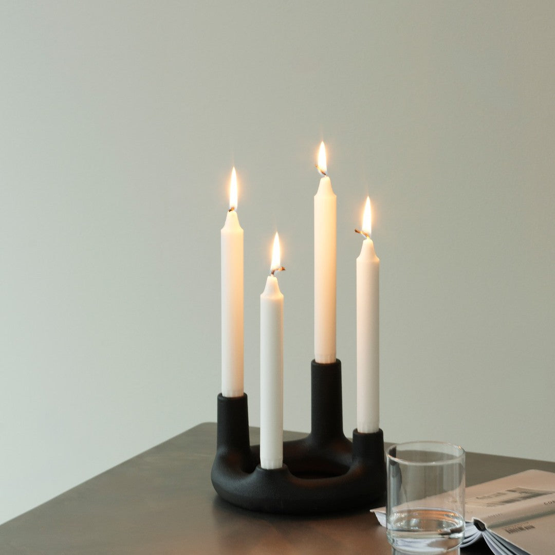 Black candle holder with four slender white candles, creating a striking contrast against a soft backdrop.