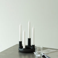 "Modern black candle holder with four white candles, minimalist design, perfect for adding elegance to any space."