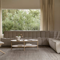 Beige sectional sofa with tufted design, paired with a white coffee table, set against a natural green backdrop.