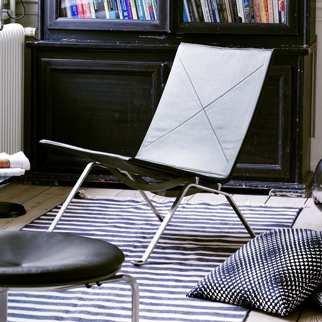 Modern gray lounge chair on striped black and white rug with patterned black cushion, set in a cozy interior.