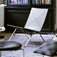 Modern gray lounge chair on striped black and white rug with patterned black cushion, set in a cozy interior.