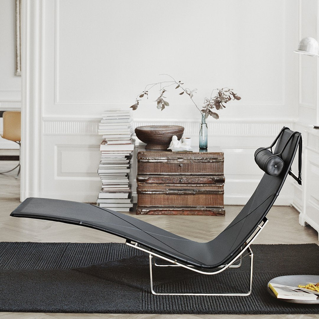 Sleek black chaise lounge with smooth curves, set against a neutral, textured backdrop and dark rug.
