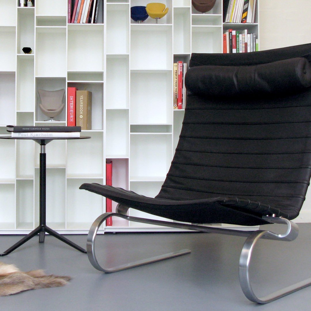 "Modern black lounge chair with horizontal striping and sleek chrome legs, set against a minimalist white bookshelf."