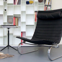 "Modern black lounge chair with horizontal striping and sleek chrome legs, set against a minimalist white bookshelf."