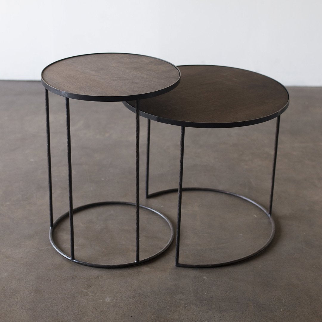 Two round side tables with dark wood tops and black metal frames, featuring a sleek, modern design.