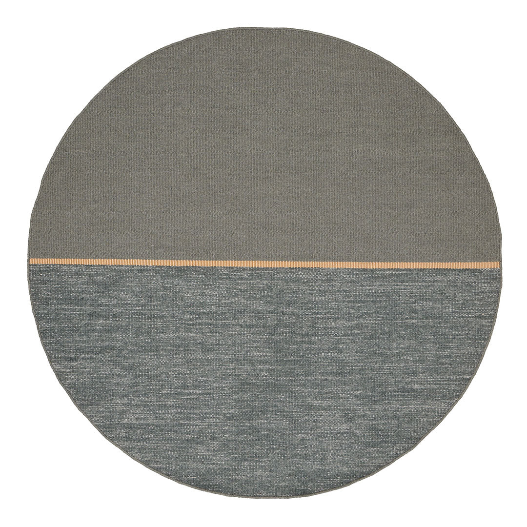 Round rug featuring a smooth gray top half and textured teal bottom half with a subtle wooden accent line.