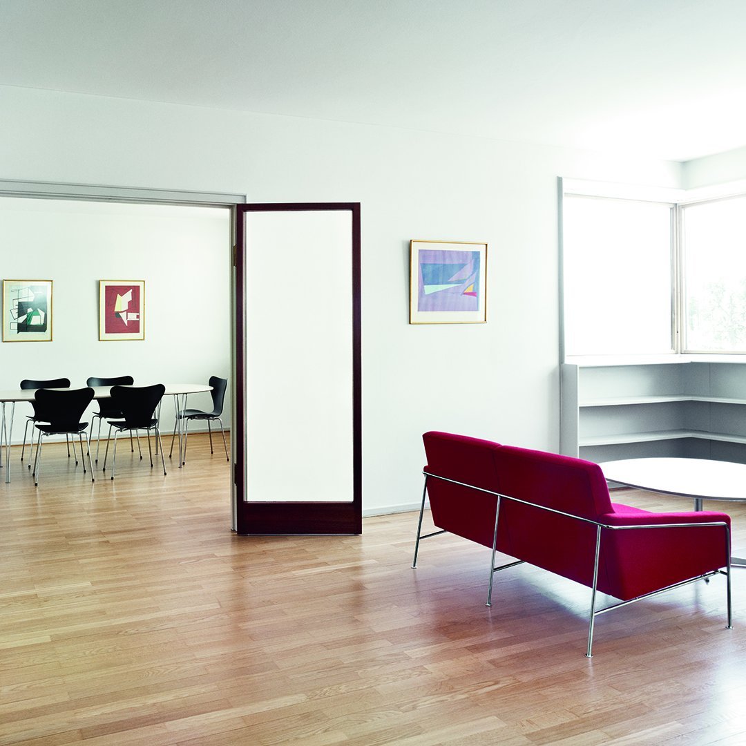 "Modern red couch on light wood floors, complemented by white walls and minimalistic black dining chairs."
