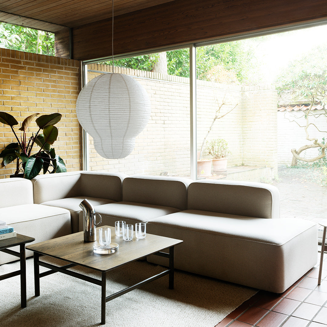 Beige modular sofa with smooth upholstery, complemented by a round white pendant light and earthy tones in the decor.