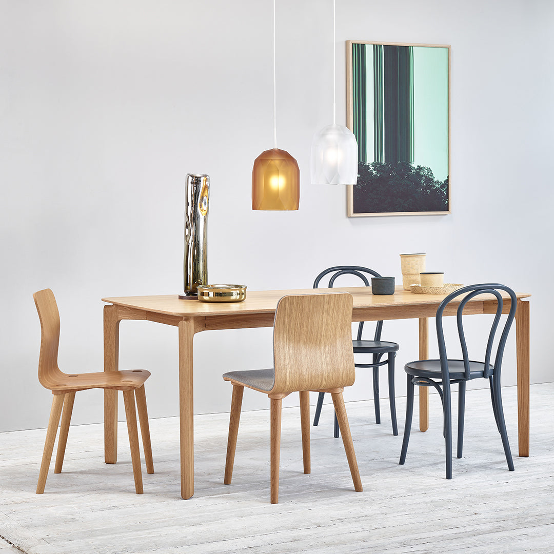 Sleek wooden dining table with natural finish, paired with black and light wood chairs and modern pendant lights.