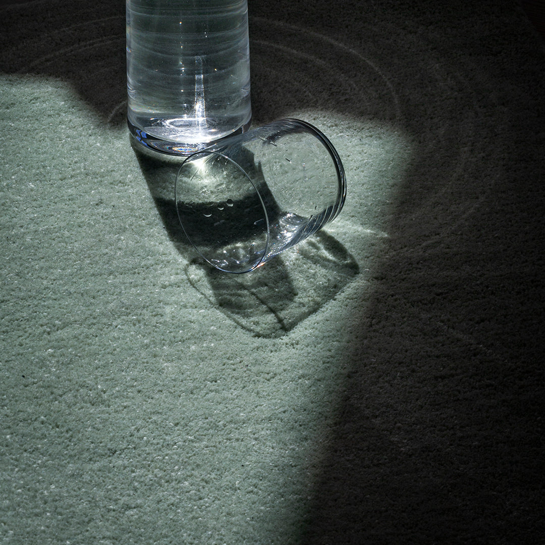 Clear glass mug casting shadows on a textured green surface illuminated by soft light.