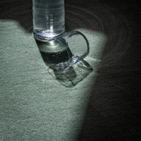 Clear glass mug casting shadows on a textured green surface illuminated by soft light.