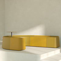 Modern yellow curved sofa with smooth, glossy finish, complemented by a minimalist round table in a neutral space.