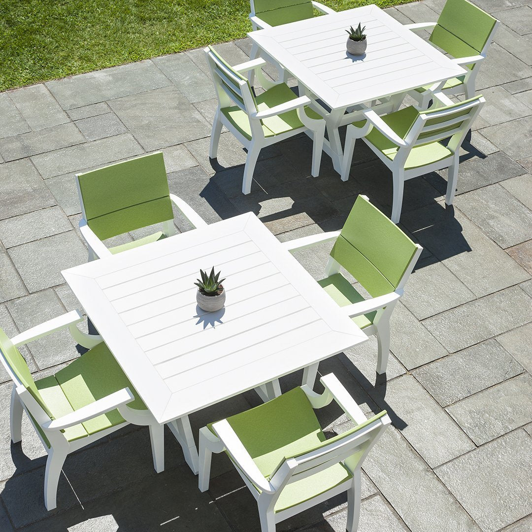 White outdoor tables and light green chairs on a stone patio with a small succulent centerpiece.