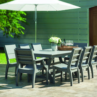 Gray outdoor dining table set with matching chairs, surrounded by greenery and a large white umbrella.