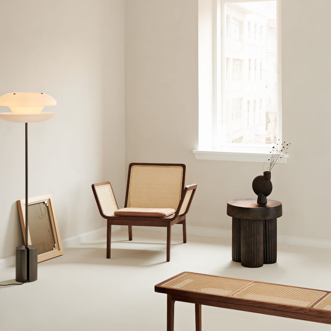 Modern wooden armchair with natural wicker accents, minimalist black lamp, and neutral beige decor. Stylish and chic.
