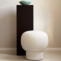 White textured pouf next to a sleek black pedestal table with a light blue bowl, showcasing a modern color palette.
