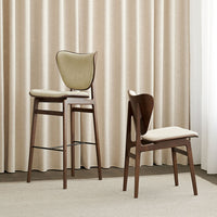 "Elegant beige and cream upholstered chairs with dark wooden frames, set against soft beige curtains."
