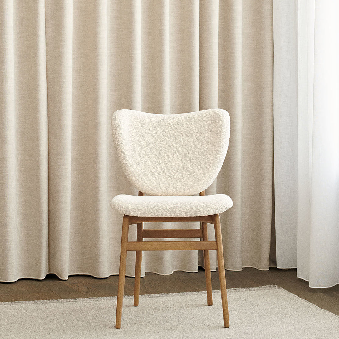 Elegant cream chair on wooden legs against textured beige curtains, perfect for modern decor.