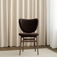 "Elegant brown upholstered chair with curved backrest against soft beige curtains and neutral-toned rug."