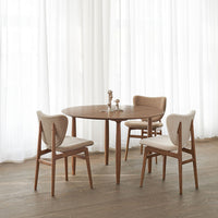 Round wooden table with beige upholstered chairs, featuring soft textures and warm tones in a light, airy setting.